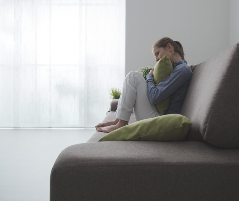 mujer triste agarrando un cojín sentada en el sofá en una habitación oscura