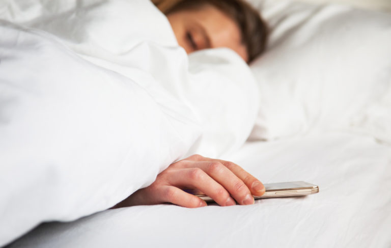 mujer en la cama con el edredon dormida con el movil en la mano