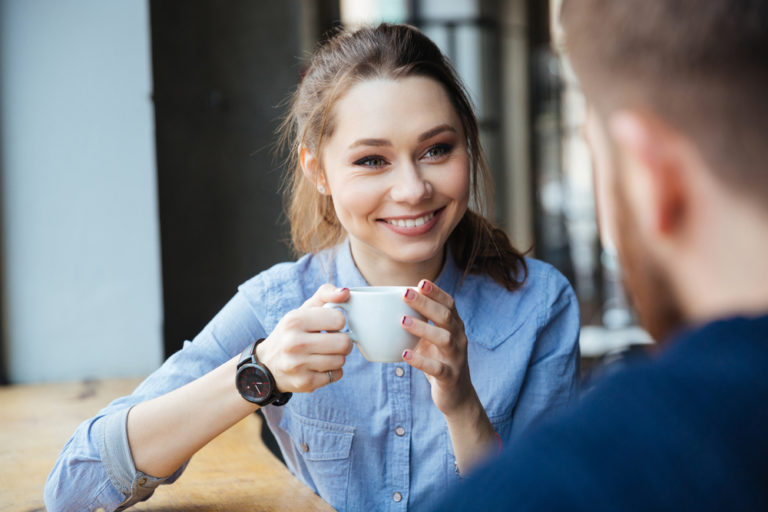 mujer feliz sonriendo vestida de azul tomando un cafe con un chico hombre de espaldas en una mesa de madera bar