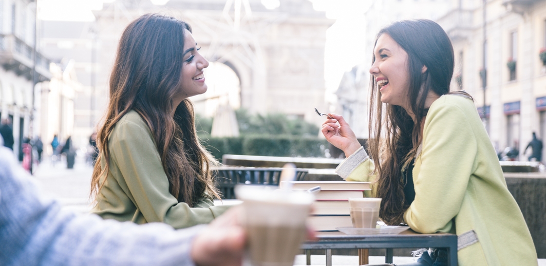 dos chicas vestidas de verde hablando riéndose y felices en un bar terraza tomando un café 