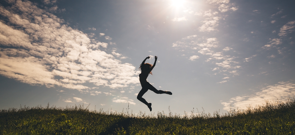mujer silueta saltando feliz bailando en el campo con el paisaje detrás sol y campo 