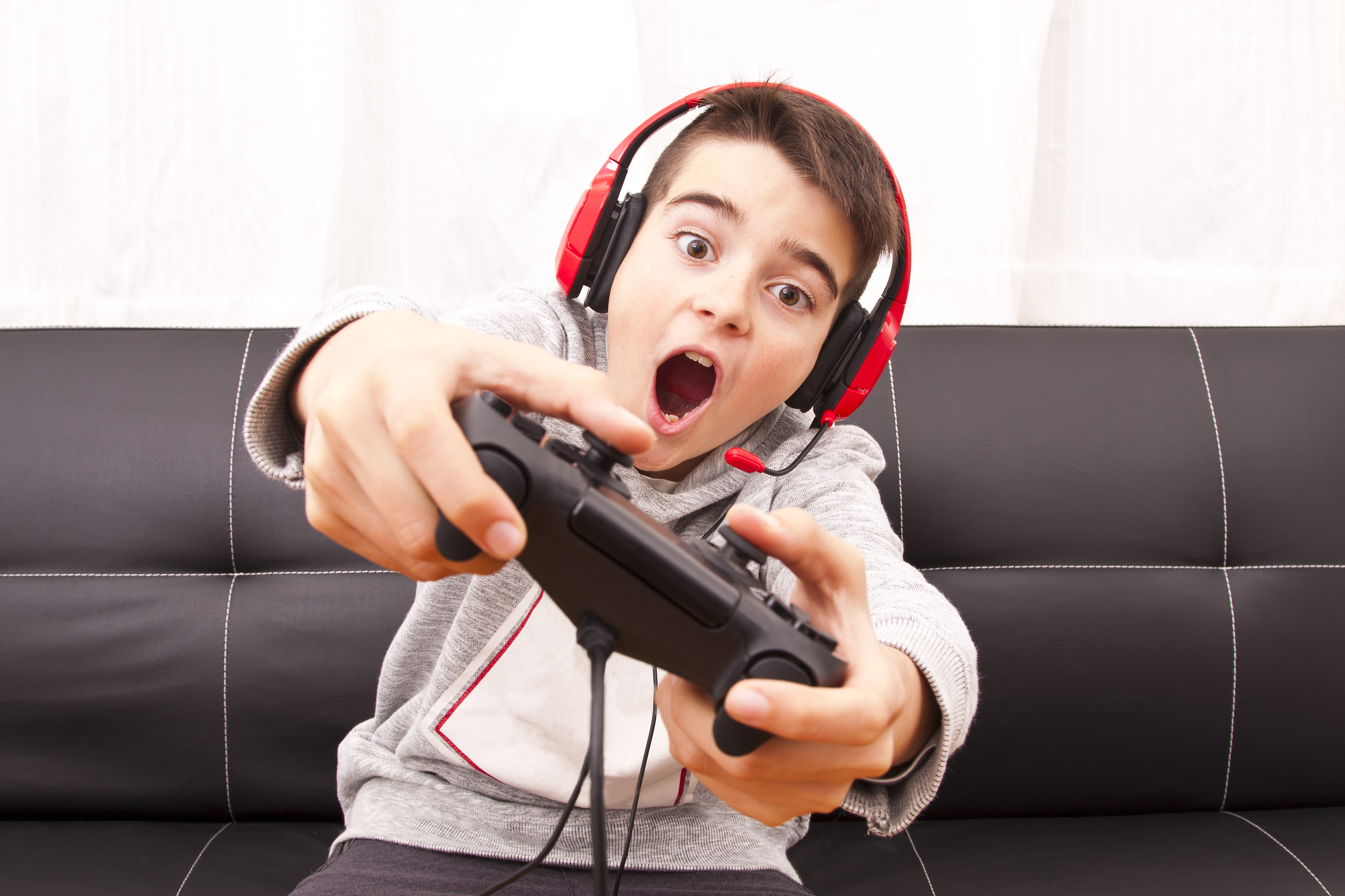 niño jugando a la consola con mando de playstation y cascos en un sofá negro